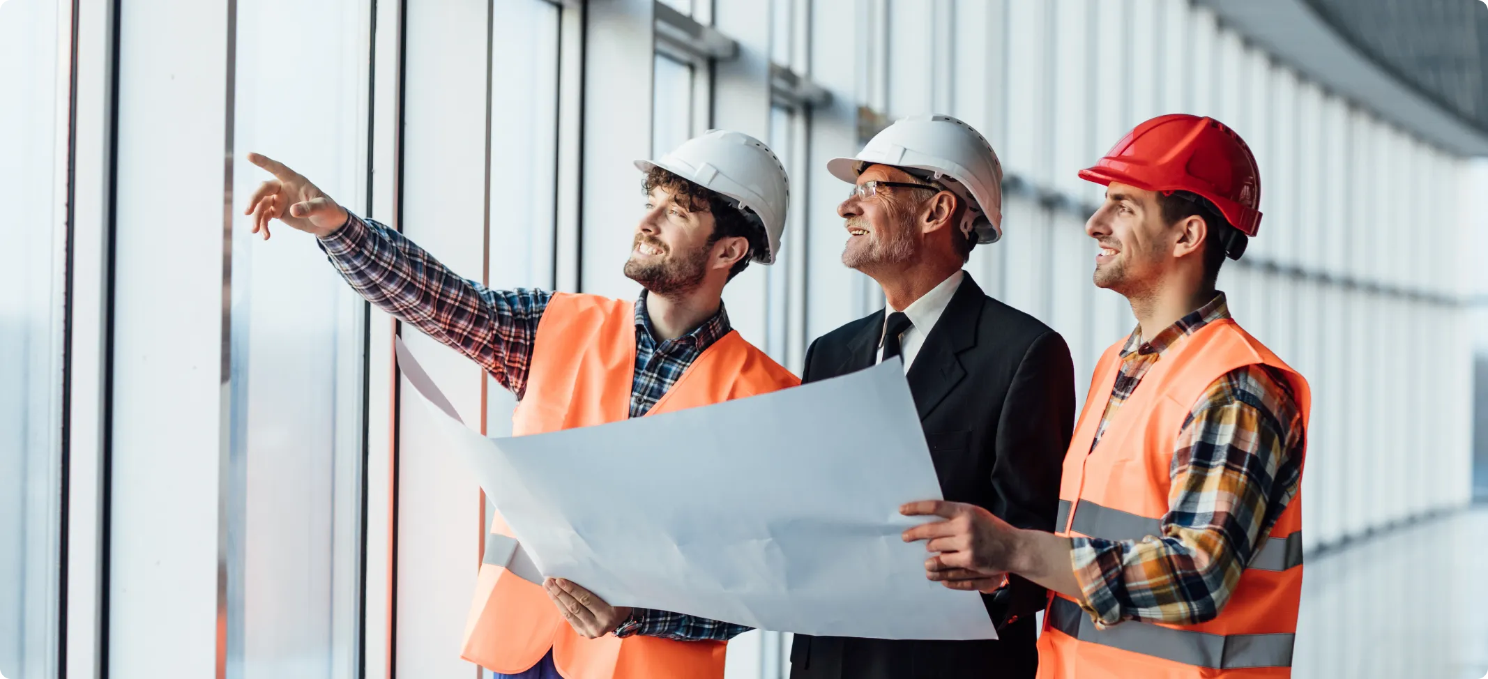 Three men in hard hats and vests looking at a blueprint.